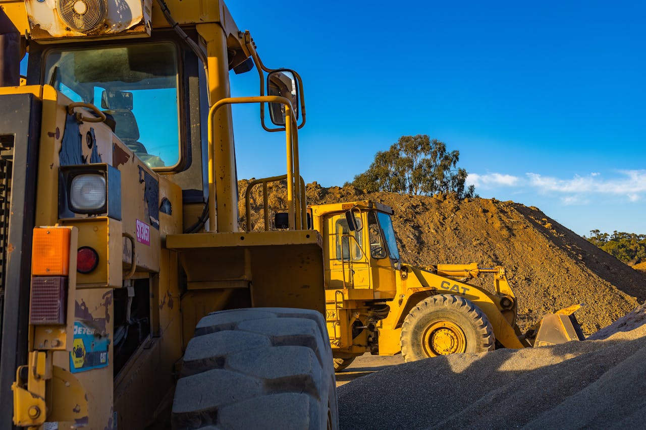 Industrial machinery operating outdoors, showcasing a bulldozer and a loader amidst piles of soil.