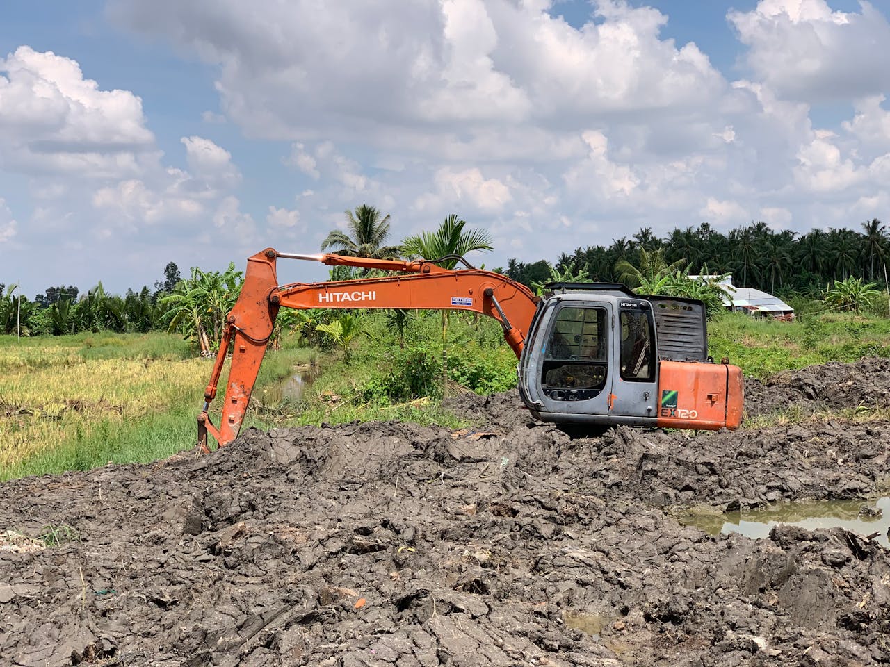 Orange excavator in a rural field under a bright blue sky, ready for earthmoving work.